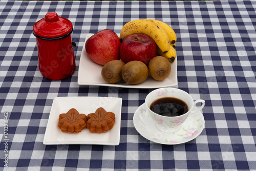 Top view of a coffee cup and a plate with two maple leaf-shaped Wagashi pastries on a navy blue and white plaid tablecloth. Ideal for autumn snack and Japanese food concept.