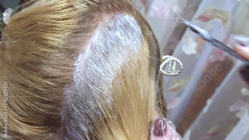 Master applying dye to the roots of a woman's light hair with a brush. Close up of the coloring procedure.