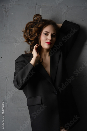 Confident woman posing elegantly in black blazer against a gray wall in a stylish indoor setting