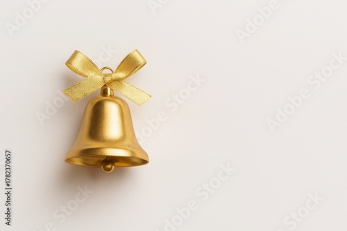 Golden Christmas bell with satin bow on cream background symbol of celebration joy and holiday tradition ideal for classic festive visuals
