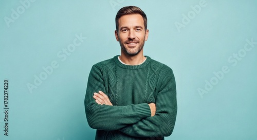 Smiling man with arms crossed wearing a green sweater on a teal background
