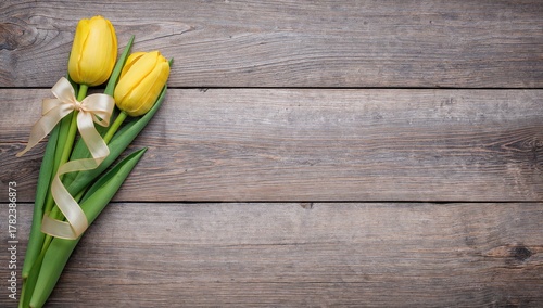 Yellow tulip adorned with ribbon and heart against a rustic wooden backdrop, ideal for a Mother's Day greeting card