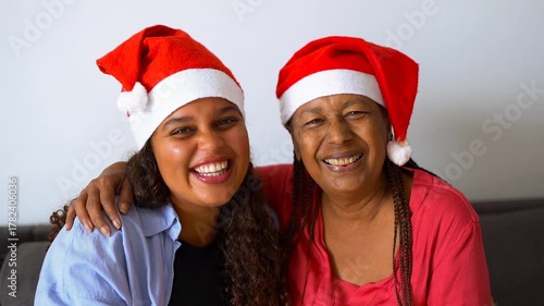 Happy african mother and daughter hugging each other while wearing Santa Claus hats during Christmas time - Family, love and Xmas concept	