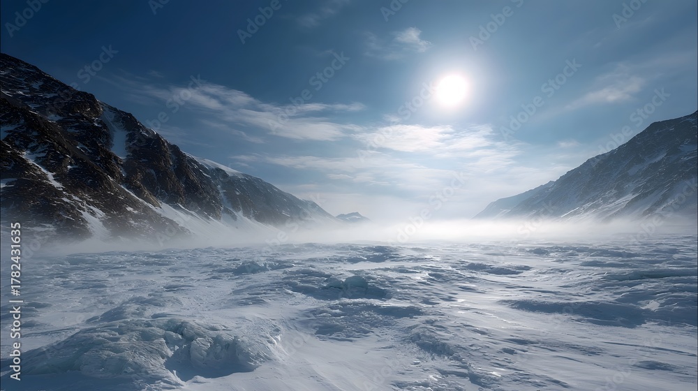 Fototapeta premium A dramatic frozen mountain landscape under a bright hazy sun with blowing snow