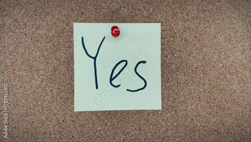 Sticky note with handwritten word YES on cork board – motivation and positive mindset concept