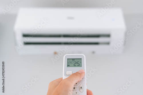 Close up of female hand using remote control to set air conditioner temperature at 25 degrees, concept of comfort, cooling and modern home technology