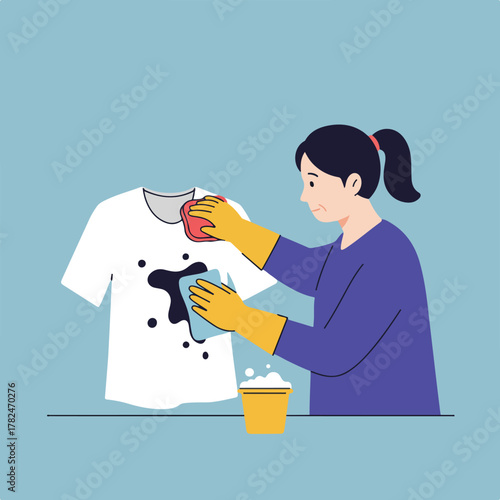 A woman cleans a white t-shirt with a dark stain using a sponge and detergent, wearing gloves