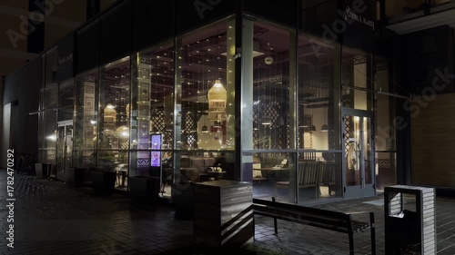 Restaurant outdoors with warm light shining through glass windows at night, cozy illuminated