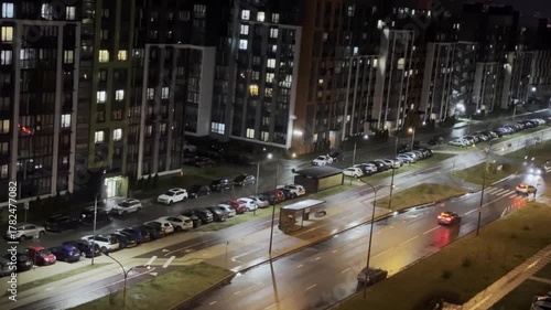 Street at night with moving cars and illuminated buildings, wet asphalt with reflections,