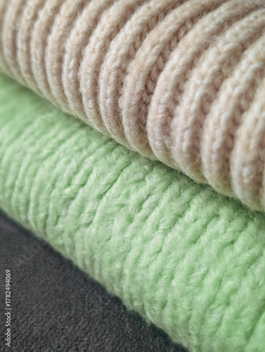 close-up stack of rolled cozy fabrics: beige ribbed knit, pale green knit and dark gray texture