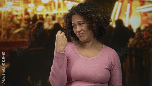 Woman pinches nose at nighttime street fair under colorful carnival lights while grimacing in front of game booths; disgust.