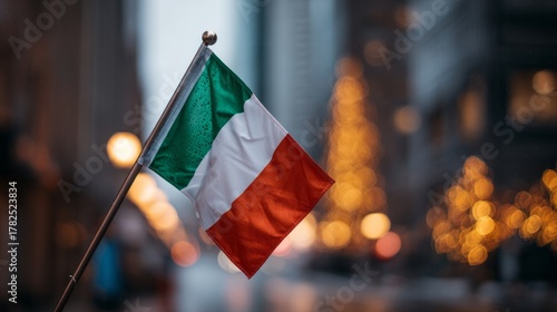 Fototapeta Naklejka Na Ścianę i Meble -  Small national banner featuring green white and red vertical stripes waves against a blurred city background