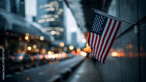 Fototapeta Naklejka Na Ścianę i Meble -  Small national banner hangs attached to an exterior wall beside a blurred city street at dusk