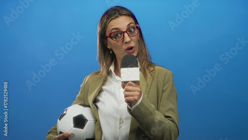 Canvastavla Woman holding microphone and soccer ball in blue studio speaking to camera; sports reporting confident