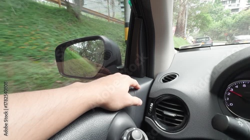 Point-of-view shot from the driver seat inside a moving car, showing a relaxed arm resting on the door near the window and the side view mirror suggesting a peaceful drive through a city