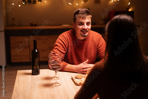 Young man and woman enjoying a romantic, drinking wine on dinner with festive lights, celebrating Valentine's Day. love