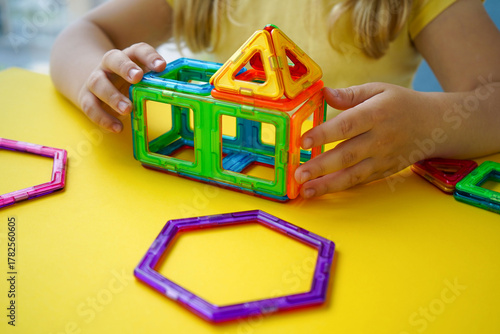 A kid experiments with spatial design using a magnetic constructor featuring colorful geometric tiles of various shapes and sizes.