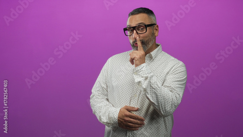 Fotografia Man wearing glasses pointing finger with clasped hands in purple studio set; confidence witty charm