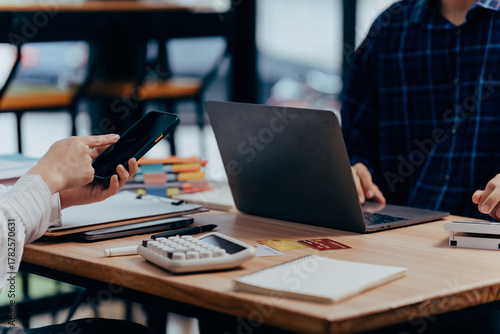 Technology Collaboration: A close-up view capturing the dynamic interaction between individuals collaborating in a modern office environment, featuring laptop and mobile.