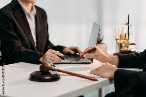Legal Agreement: Two figures collaborate over contract document, a gavel in the foreground symbolizes legal action, while a laptop rests nearby symbolizing modern communication.