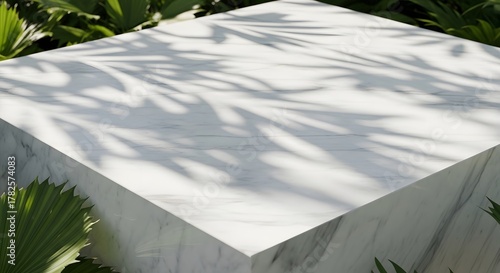 White marble cube platform with palm leaf shadows and green foliage in background