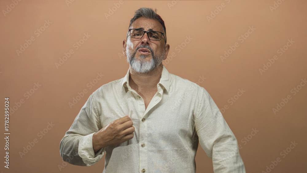 Fototapeta premium Man middle aged gesturing with hands and adjusting shirt collar in studio with peach backdrop; frustration self reflection.