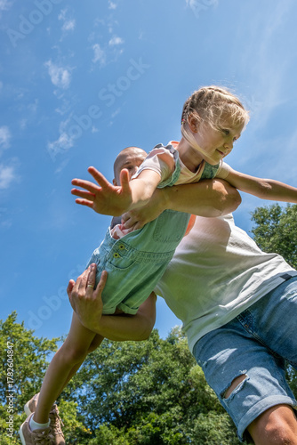 Foto Father lifting daughter joyfully in a sunny park, showcasing their playful bond