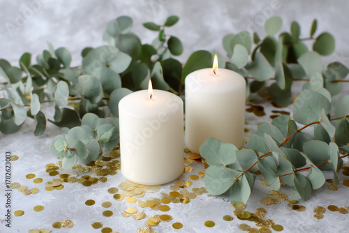 Eucalyptus leaves, burning candles, and gold confetti on white surface