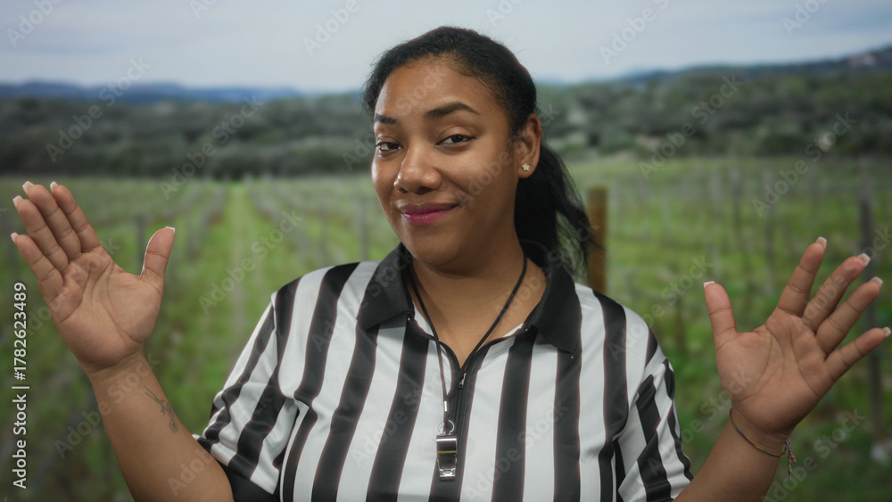 Obraz premium Woman referee in striped shirt smiles and raises palms gesture with whistle at neck in forest clearing; serenity.