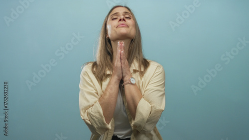 Photography Woman with blonde hair praying with hands pressed together in studio against a light blue background; devotion