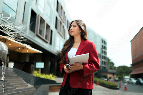 Young Asian businesswoman holding tablet walking city street