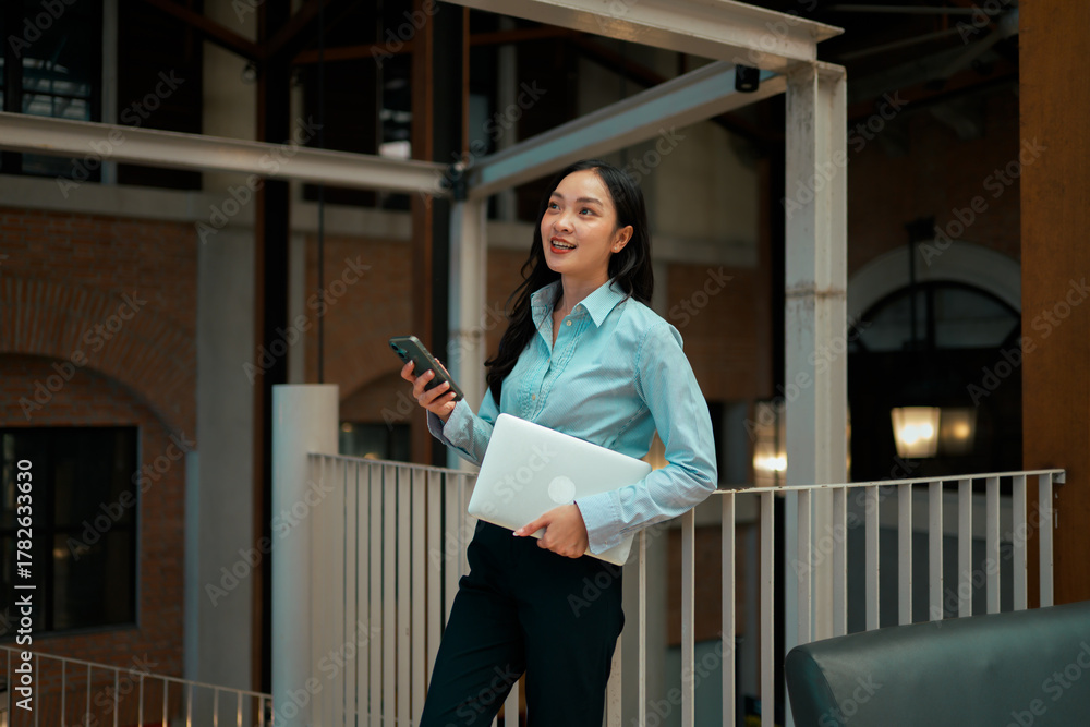 Fototapeta premium Asian businesswoman multitasking, holding laptop and smartphone in modern office