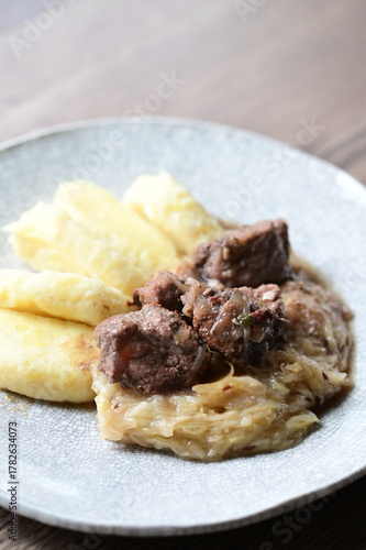 traditional Czech cuisine, wild boar pork belly with sauerkraut and potato dumplings, served meal on a white plate, authentic restaurant food, hearty comfort dish,