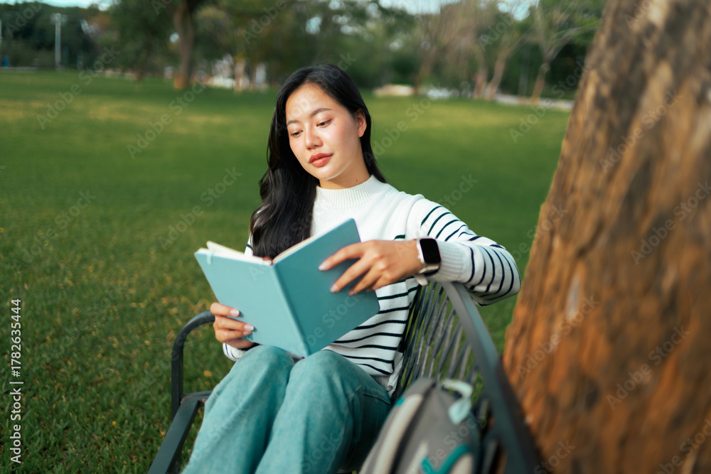 Fototapeta premium Young woman student reading book in green park