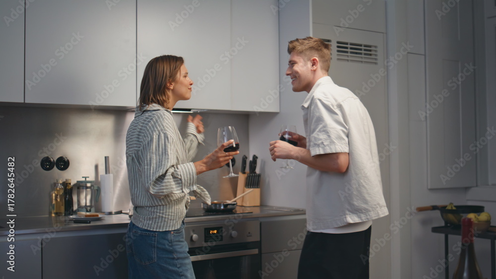 Fototapeta premium Cheerful spouses dancing kitchen with wine glasses. Carefree husband cooking