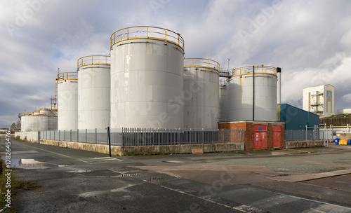 Industrial Storage Tanks Complex With Large White Silos, Fenced Yard, and Brick Utility Buildings