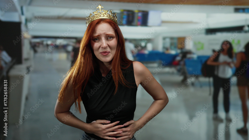 Fototapeta premium Woman with crown looking distressed at airport terminal suggesting travel discomfort amid crowded indoor setting.