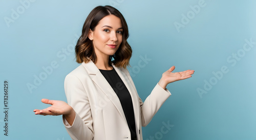 Charming young woman in a blazer with an open hand gesture, posing confidently and inviting interaction or decision on a blue background