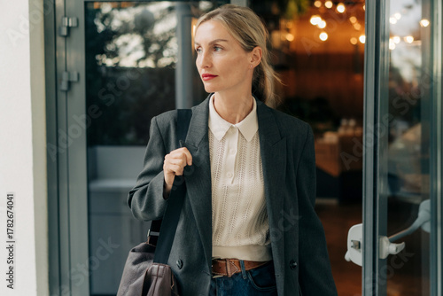 Professional woman in a blazer walking out of a restaurant with a bag and smart casual attire