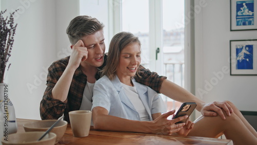 Smiling couple using cellphone indoors. Sweethearts enjoying moment together