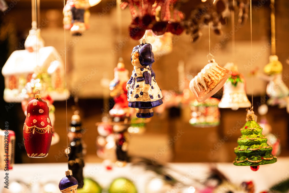 Marché de Noël en Alsace, décorations suspendues sur un stand, boules en forme de personnages et objets traditionnels, éclairage chaleureux 