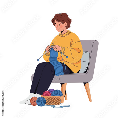 Woman knitting a blue scarf while sitting in a chair with yarn basket.