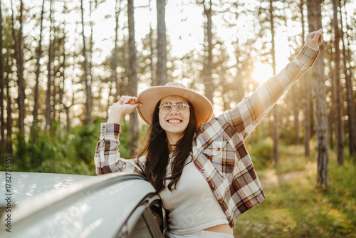 Young caucasian woman sitting on a car window in the forest enjoying nature during golden hour