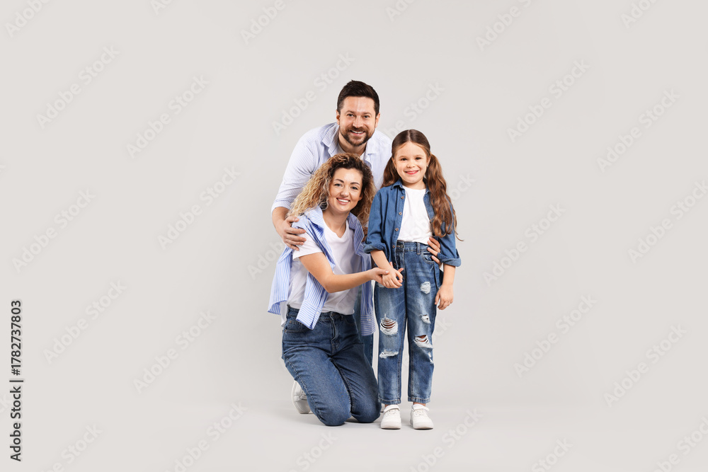 Fototapeta premium Happy parents and their daughter hugging on grey background. Family bonding
