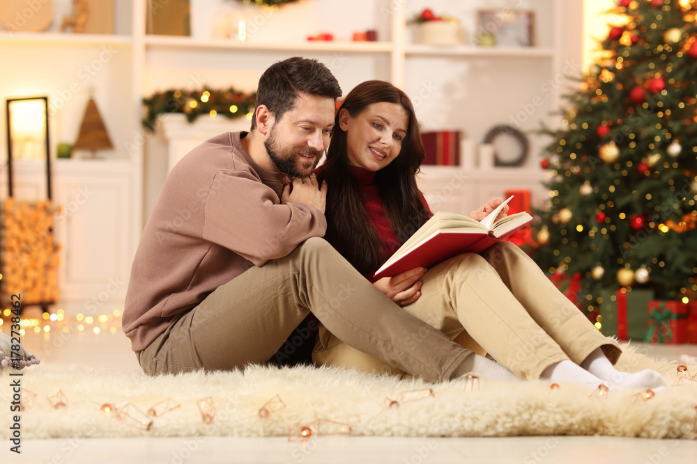 Obraz premium Happy couple reading book together in room decorated for Christmas