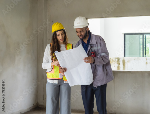 construction site scene two engineer engaged talk. wearing safety helmet reflective vest, hand holding blueprint,while listen attentively. background show part concrete structure