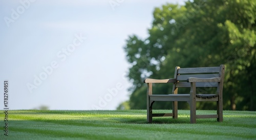 Fototapeta Naklejka Na Ścianę i Meble -  Wooden bench on green lawn under blue sky. Serene outdoor scene for rest, leisure, and relaxation.