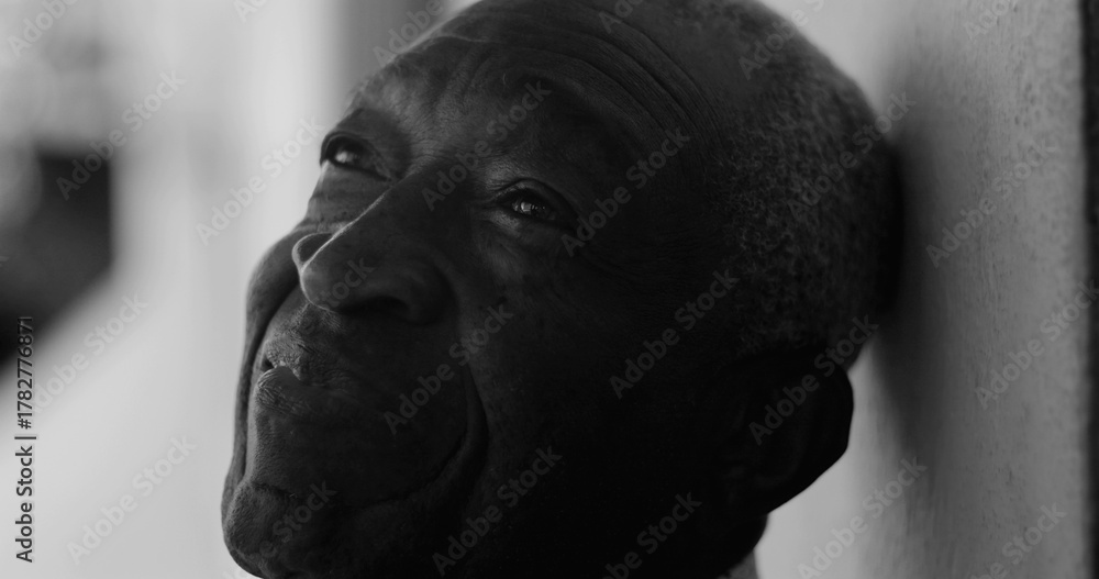 Fototapeta premium African American elderly man gazing upward with a serene expression, leaning against a wall in black and white, exuding calmness, wisdom, and introspection