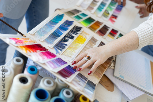 Hands choosing textile color shades in creative workspace. Collaboration, aesthetic decision, and teamwork in modern fashion design.