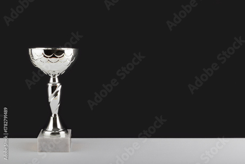 Silver winner cup on white table against black wall background.